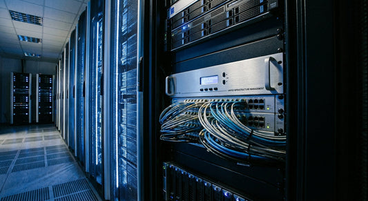 A hardware KVM switch mounted in a server rack inside a professional data center, with organized cables and cool blue ambient lighting.